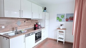 Cocina moderna con armarios blancos, pileta de acero inoxidable, un hervidor rojo y un estante pequeño blanco con utensilios de cocina.