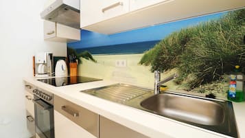Een koelkast, een oven, een vaatwasser, kookgerei, borden en bestek