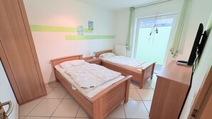 Una habitación con dos camas de madera, un escritorio pequeño y una ventana con persianas.