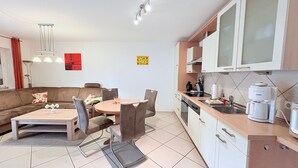 Una cocina moderna con armarios blancos, un comedor con una mesa redonda y sillas, y una sala de estar con sofá y una mesa de centro.