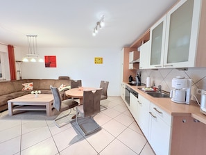 Une cuisine moderne avec des meubles blancs, un coin repas doté d’une table ronde et de chaises, et un salon avec un canapé et une table basse.