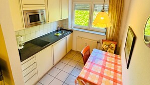 Una cocina compacta con armarios blancos, microondas, pileta y ventana con persianas.