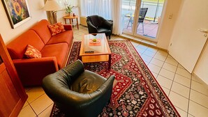Una sala de estar con un sofá rojo, un sillón de cuero negro, una mesa de centro de madera y una alfombra estampada.