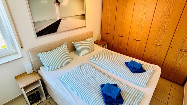 Habitación de hotel con cama, armario de madera, mesita de noche e imagen en un marco en la pared.