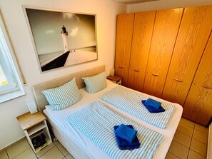Hotellihuone, jossa on sänky, puinen vaatekaappi, yöpöytä ja seinällä oleva kehystetty kuva.