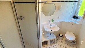 Un baño con ducha, lavamanos, inodoro y ventana con vistas.