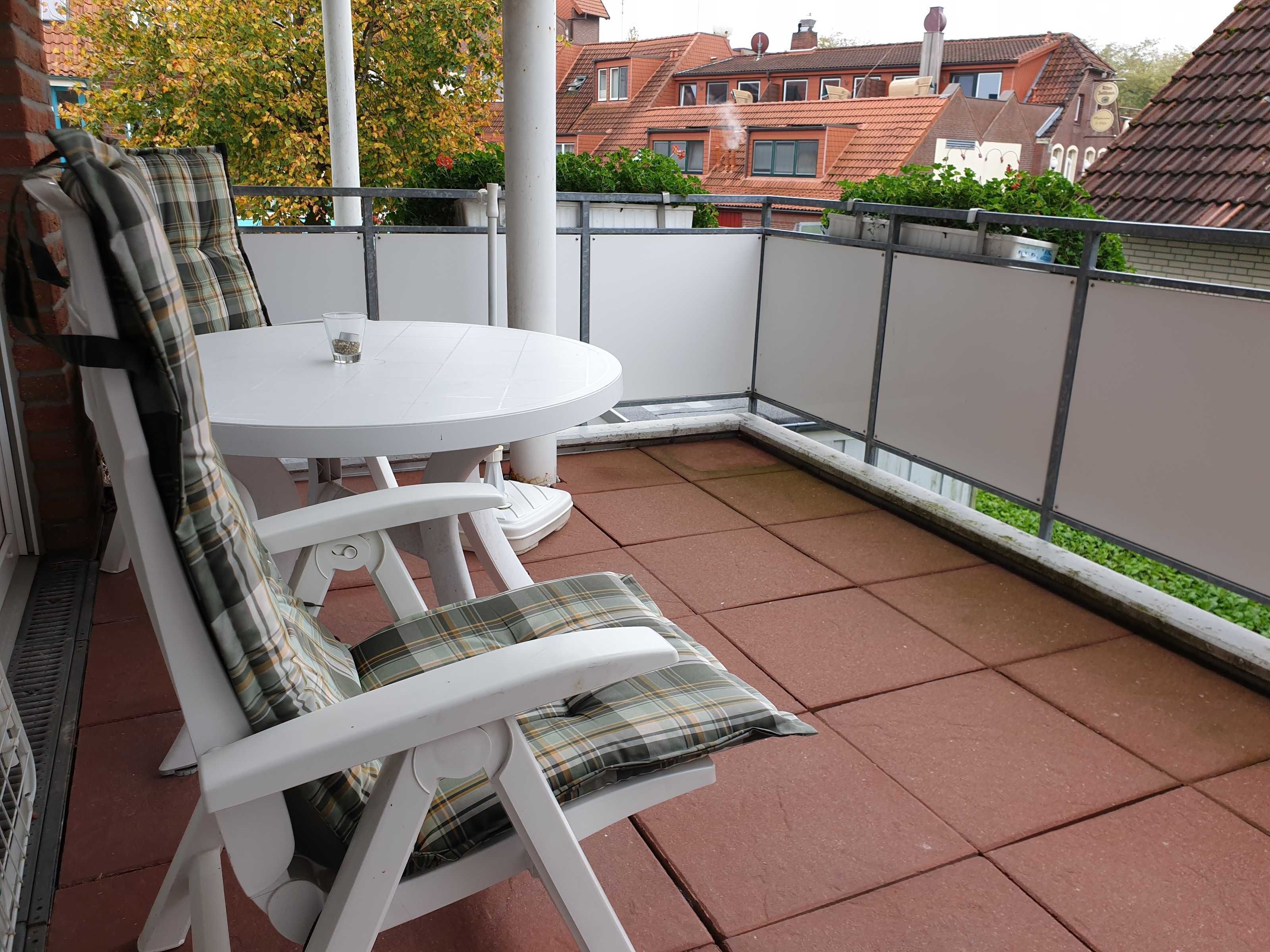 A balcony with a white table and chairs, a metal railing, and a view of buildings in the background.