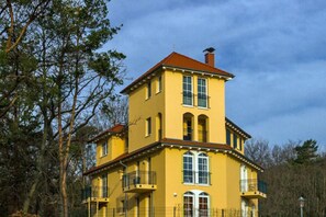 Una casa amarilla de dos pisos con techo rojo, rodeada de árboles.