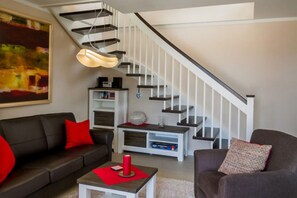 A modern living room with a staircase, a sofa, a coffee table, and a bookshelf.