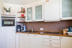 Una cocina moderna con gabinetes blancos, horno empotrado, cafetera y pileta.