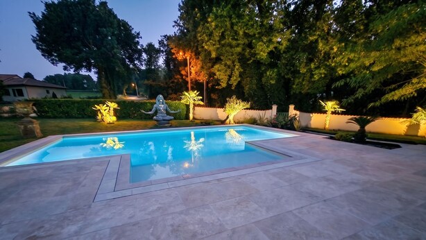A swimming pool with a meditative statue, surrounded by a landscaped garden with trees and illuminated plants. - Homerez - Villa in Ribérac (Ribérac)