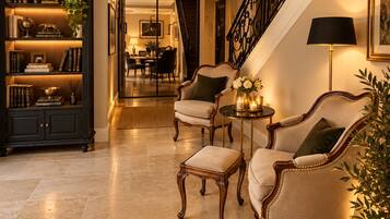 A well-lit foyer with a staircase, a bookshelf, two armchairs, and a small table with candles.