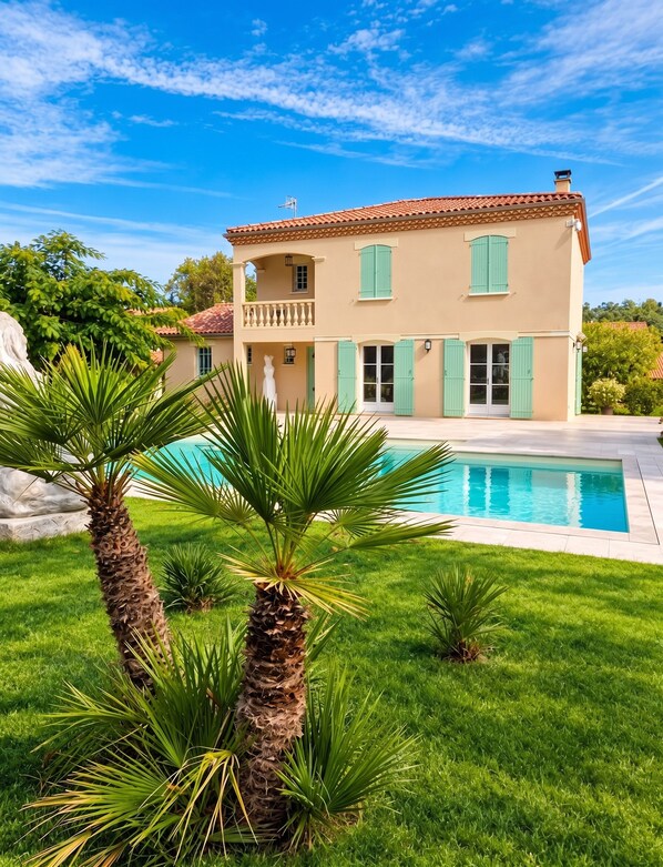Une maison à deux étages avec une piscine, entourée d’une pelouse verdoyante et de palmiers.