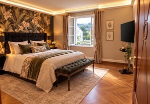 A well-appointed bedroom with a large bed, a bench, a television, and a window with curtains.