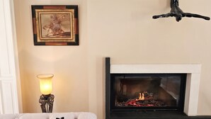 A living room with a fireplace, a sofa with patterned cushions, a framed picture on the wall, and a floor lamp. - Homerez - Villa in Ribérac (Ribérac)