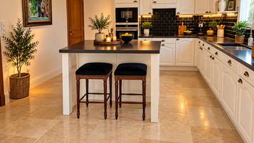 A modern kitchen with a central island, pendant lighting, and a dining area with two chairs.