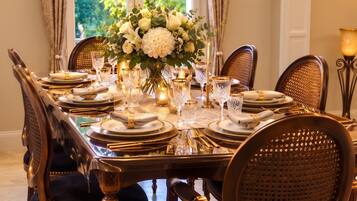 Un comedor formal con una mesa grande dispuesta para una comida, rodeada de sillas tapizadas con respaldo trenzado.