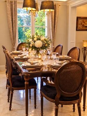 A formal dining room with a large table set for a meal, surrounded by upholstered chairs with a woven backrest.