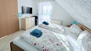A bedroom with two beds, a TV, a wardrobe, and a window with curtains. - Achtern 8 - 70018, Germany (Wangerland)