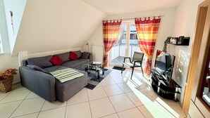 A modern living room with a grey sofa, red cushions, a glass coffee table, and a TV. - Achtern 8 - 70018, Germany (Wangerland)