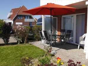 Un espace patio avec des sièges d’extérieur, un parasol rouge et une vue sur un bâtiment à la façade en briques.