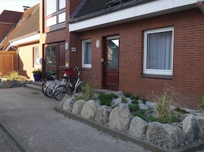 Un immeuble résidentiel à la façade en briques, portant le numéro 33, avec une porte d’entrée, des fenêtres et un petit jardin agrémenté de rochers et de plantes.