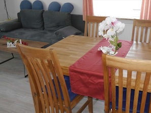 Un coin repas avec une table en bois, une nappe rouge et deux chaises en bois.
