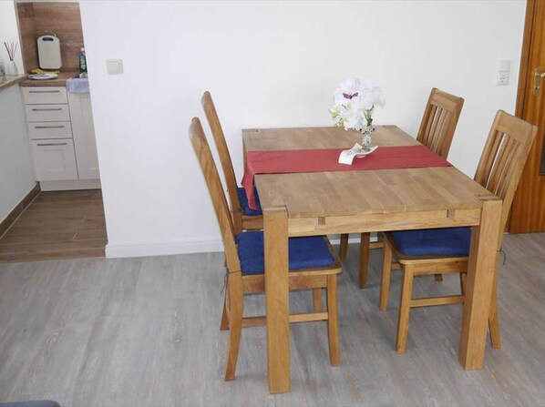 Un coin repas avec une table en bois, des chaises à l’assise rembourrée de tissu bleu et un chemin de table rouge.