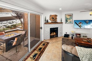 A living room with a fireplace, a TV, and a glass door leading to an outdoor area with a fire pit. - Beautiful Townhouse! Walking Distance to Bear Mtn and Golf Course! Walk to Hiking! (Big Bear Lake)