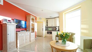 A modern living room with a television, dining table, and kitchen in the background. - Dune Residence Bansin - Apartment B 03 (Heringsdorf)