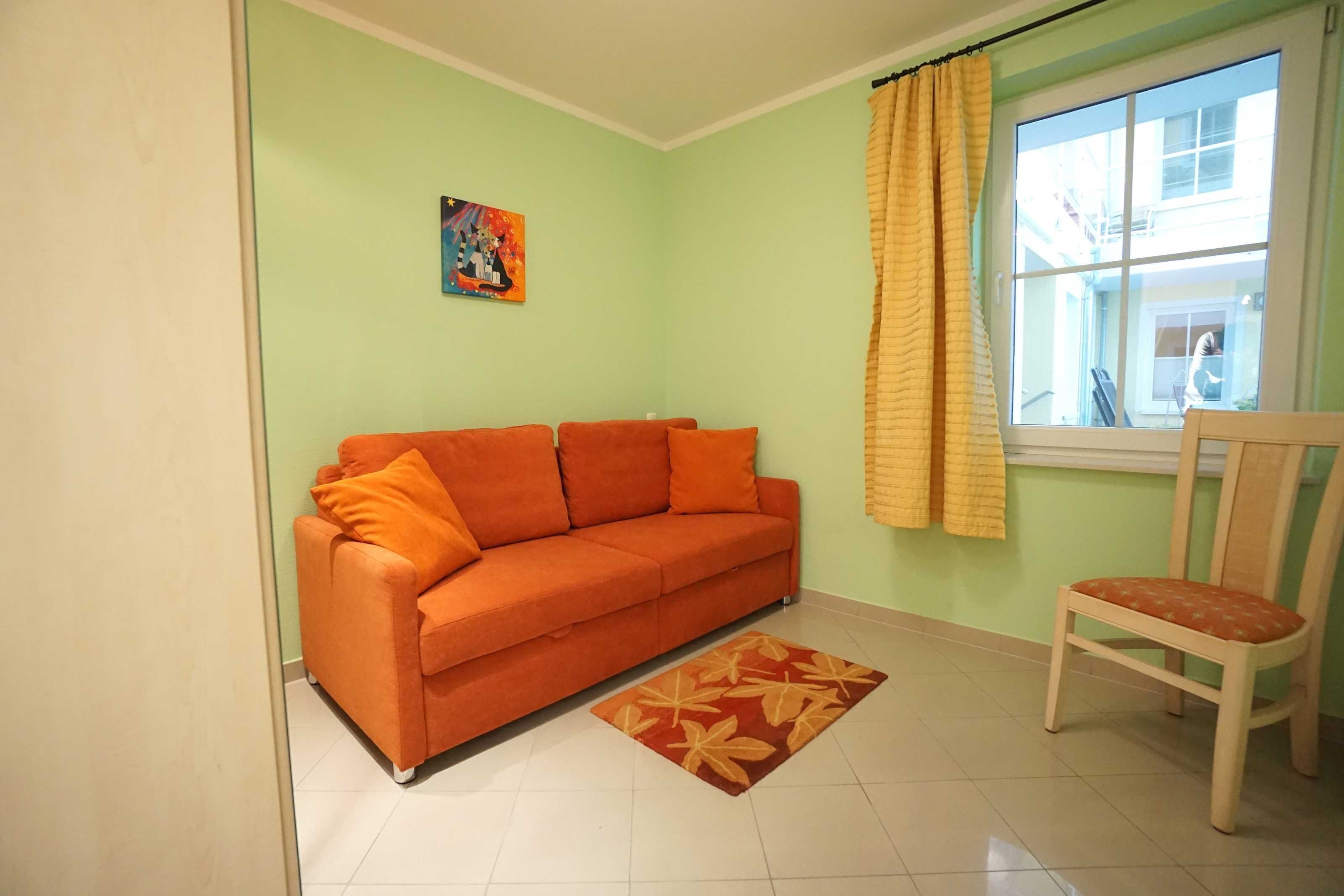 Une pièce comprenant un canapé, un fauteuil, une fenêtre avec des rideaux et un tableau accroché au mur.