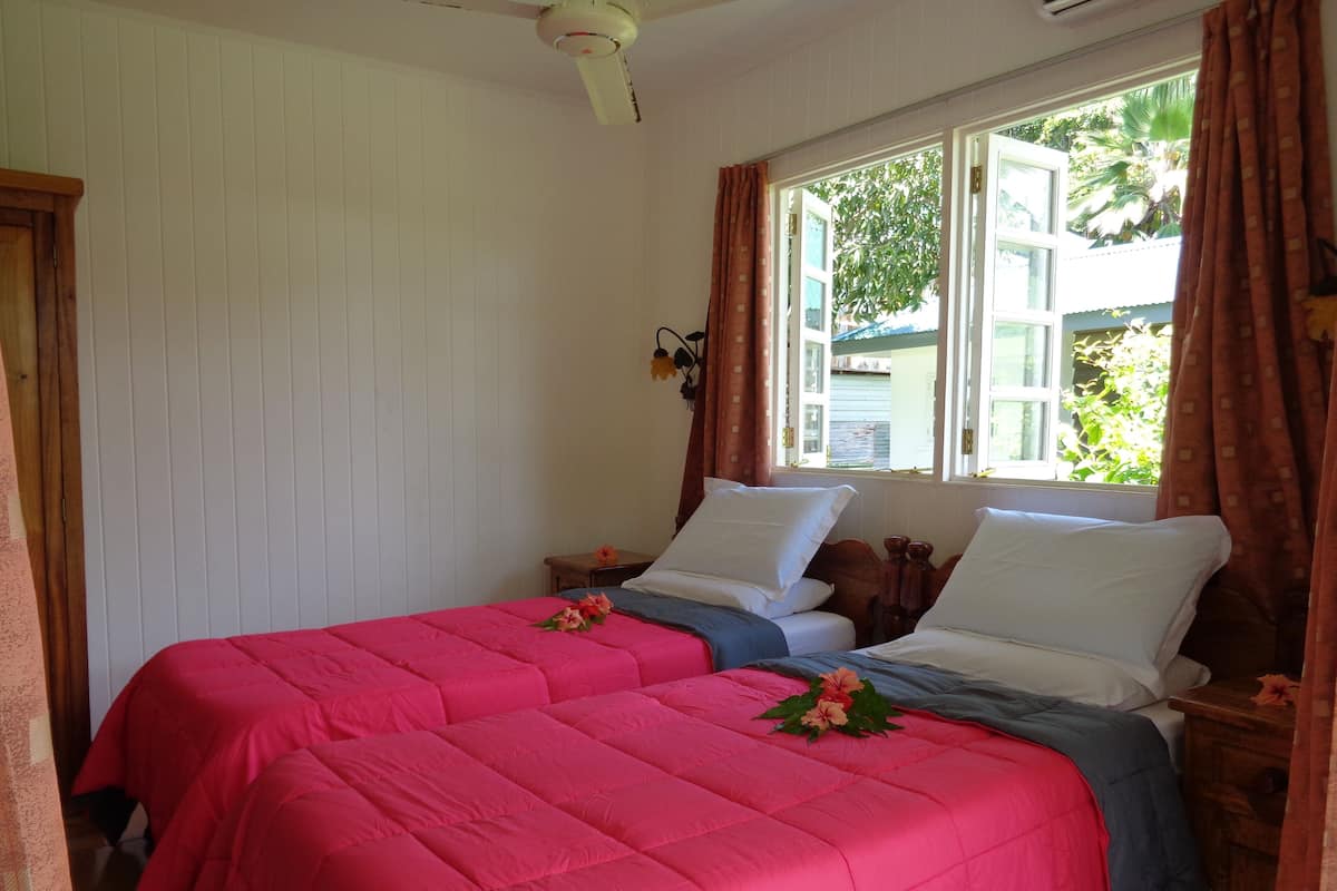 A room with two beds, white walls, a window with curtains, and a ceiling fan.
