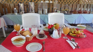 A breakfast table set with various dishes, including fruits, bread, and beverages, in a tent-like structure. - Chez Michelin Pension Residence (La Digue)