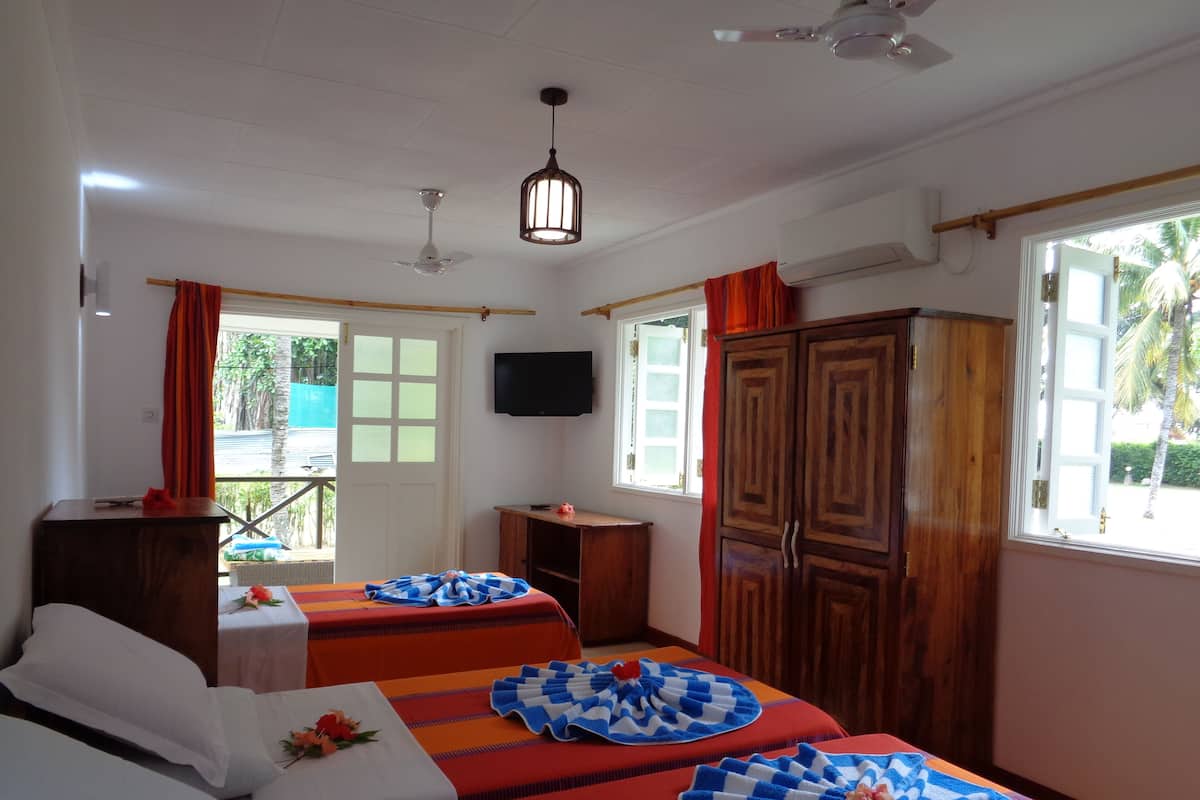 A hotel room with two beds, a wooden wardrobe, a television, and a window with curtains.