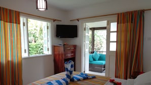 A hotel room with a bed, a television, a wooden cabinet, and a view of the outdoors. - Chez Michelin Pension Residence (La Digue)