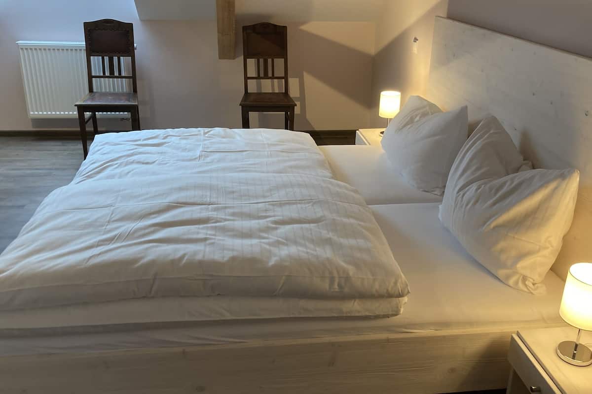 Cama bem arrumada com lençóis brancos em quarto com cabeceira de madeira e duas luminárias de apoio.