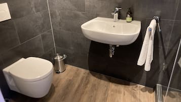 Un baño moderno con inodoro blanco, lavamanos y ducha.