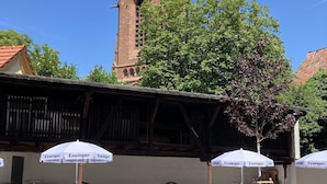 A courtyard with outdoor seating, umbrellas, and a church tower in the background. - BürgerhausLöwen (Philippsburg)