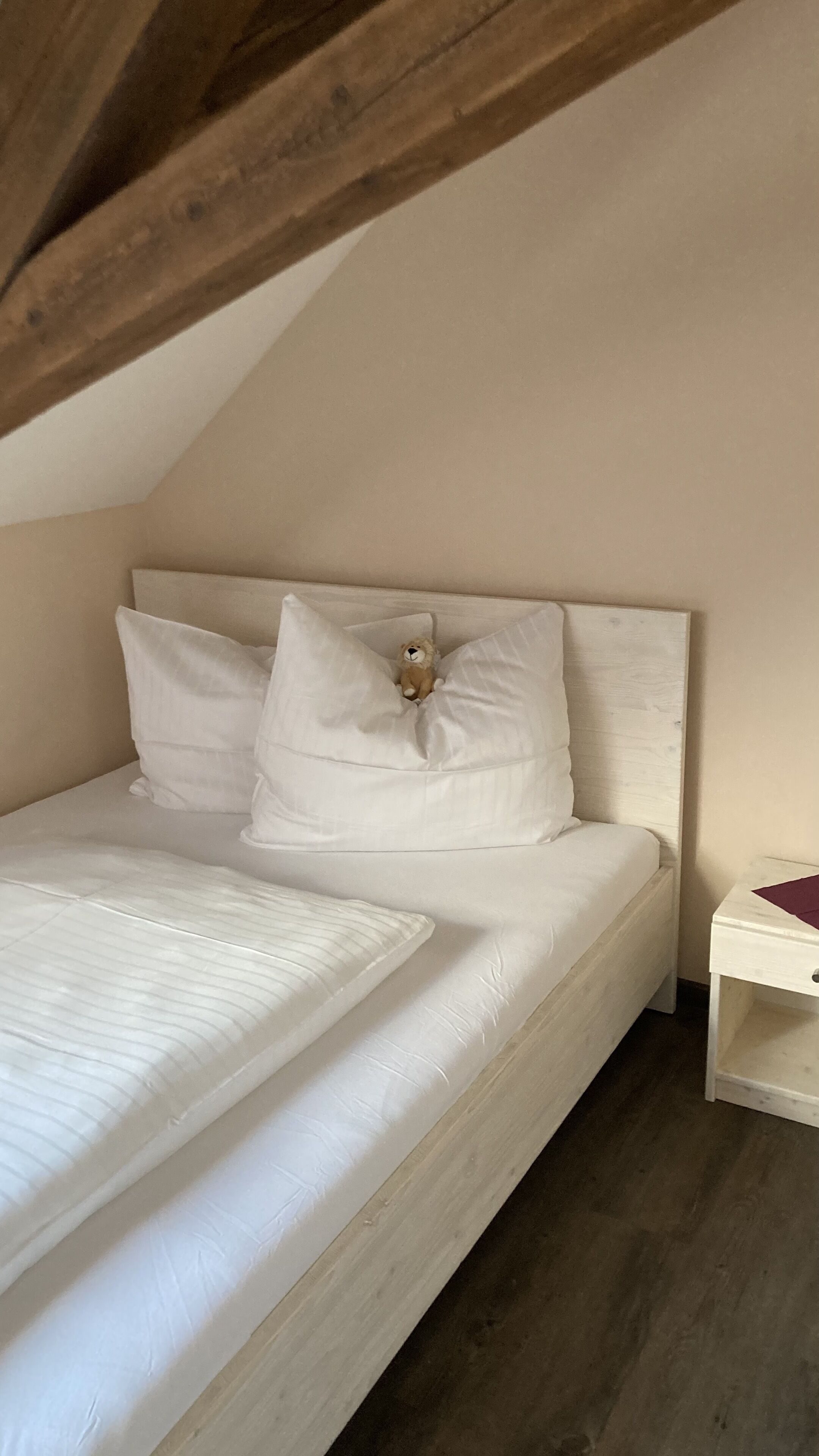 Ein Schlafzimmer mit Holzboden, einem Bett mit weißer Bettwäsche und einem Nachttisch mit einem roten Gegenstand darauf.