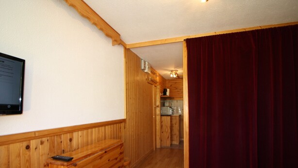 A wooden interior with a bench, a bed, and a kitchen area visible through an open door. - Classic studio for 2 in Tignes (Tignes)
