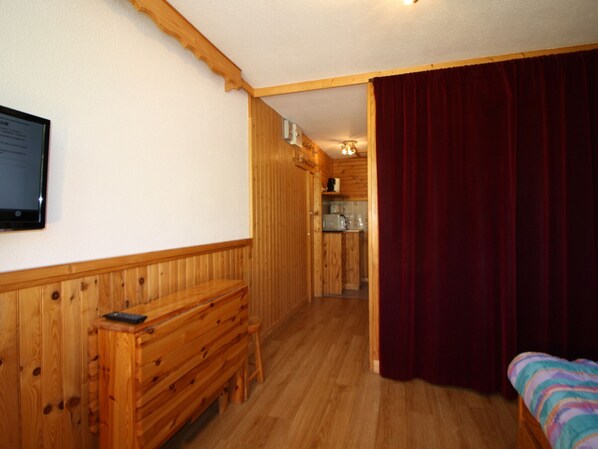 Un intérieur en bois avec un banc, un lit et un coin cuisine, visibles à travers une porte ouverte.
