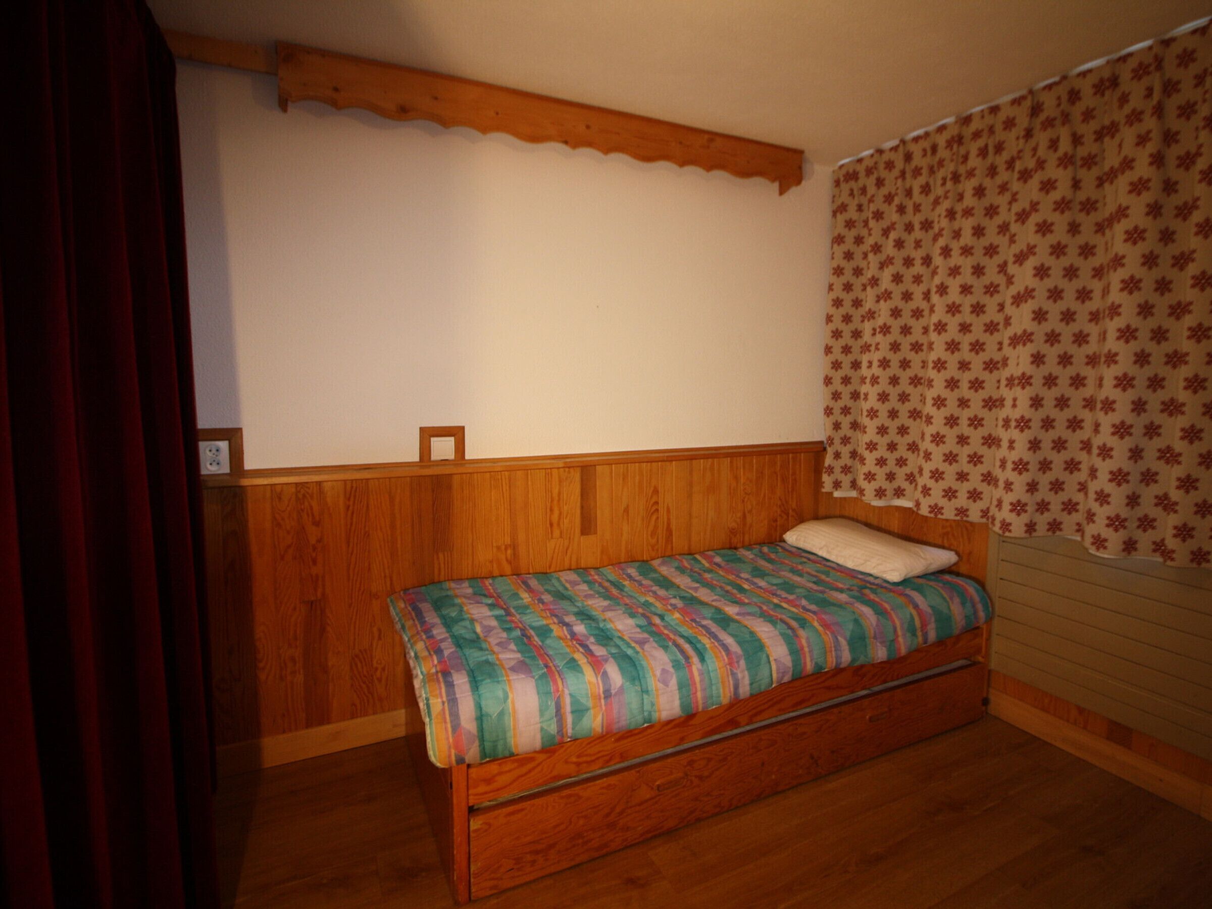 Una habitación pequeña con cama individual, cabecera de madera y colcha a rayas sencillas.