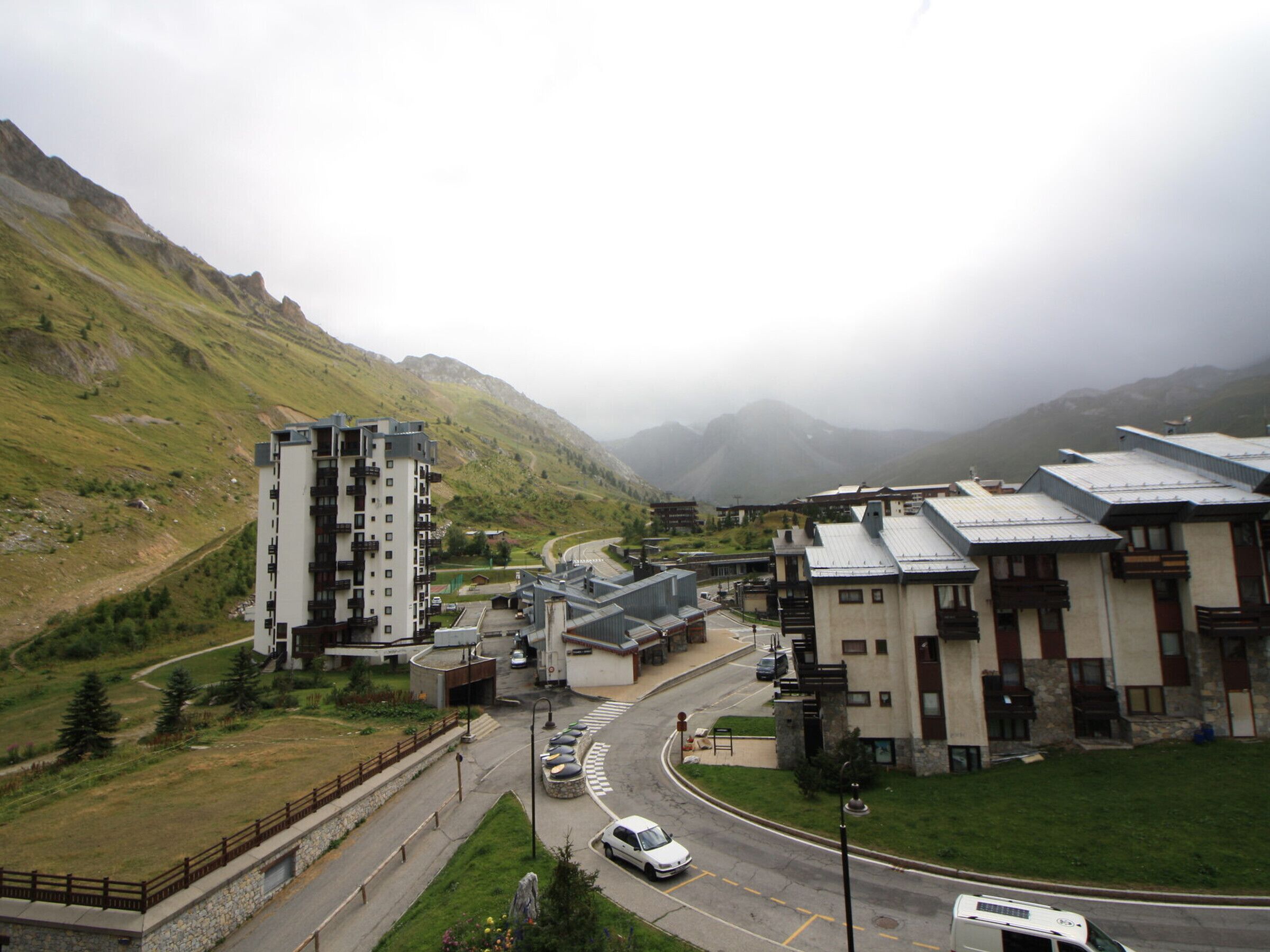 A modern hotel with multiple floors, a parking area, and a view of surrounding mountains.