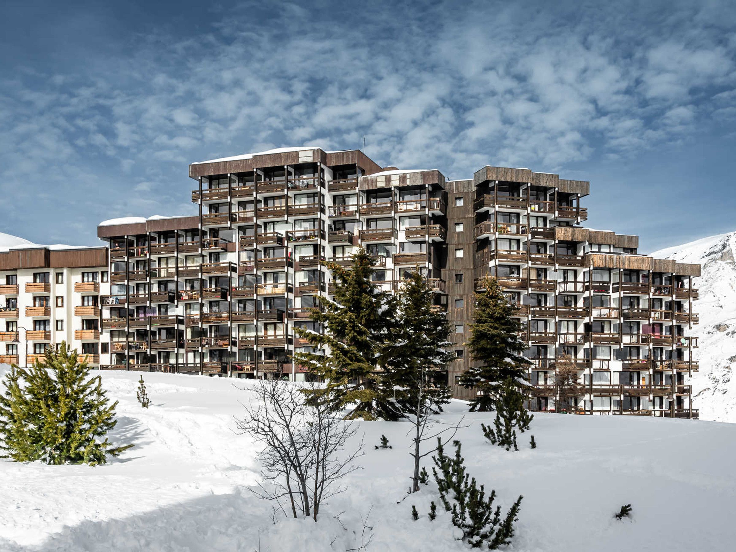 A multi-story hotel with balconies, set against a snowy mountain backdrop.