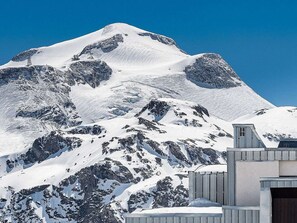 Une montagne enneigée sur laquelle se dresse un bâtiment moderne, doté d’un toit en pente et d’une petite entrée.