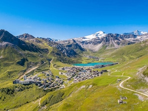 A mountainous landscape with a town nestled in a valley, featuring a lake and snow-capped peaks in the background.