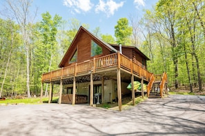 A wooden cabin with a balcony, a covered porch, and a staircase leading to the upper level.