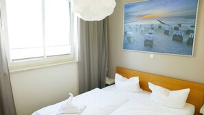Ett hotellrum med en stor säng, en tavla som föreställer en strandscen och ett fönster med gardiner.