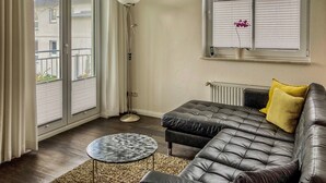 Ett vardagsrum med en soffa, ett litet runt bord, en golvlampa och ett fönster med persienner.