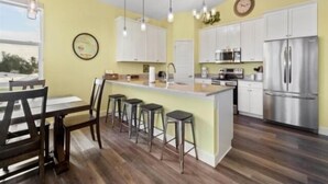 Una cucina moderna con mobili bianchi, elettrodomestici in acciaio inossidabile e un'isola centrale con sgabelli.